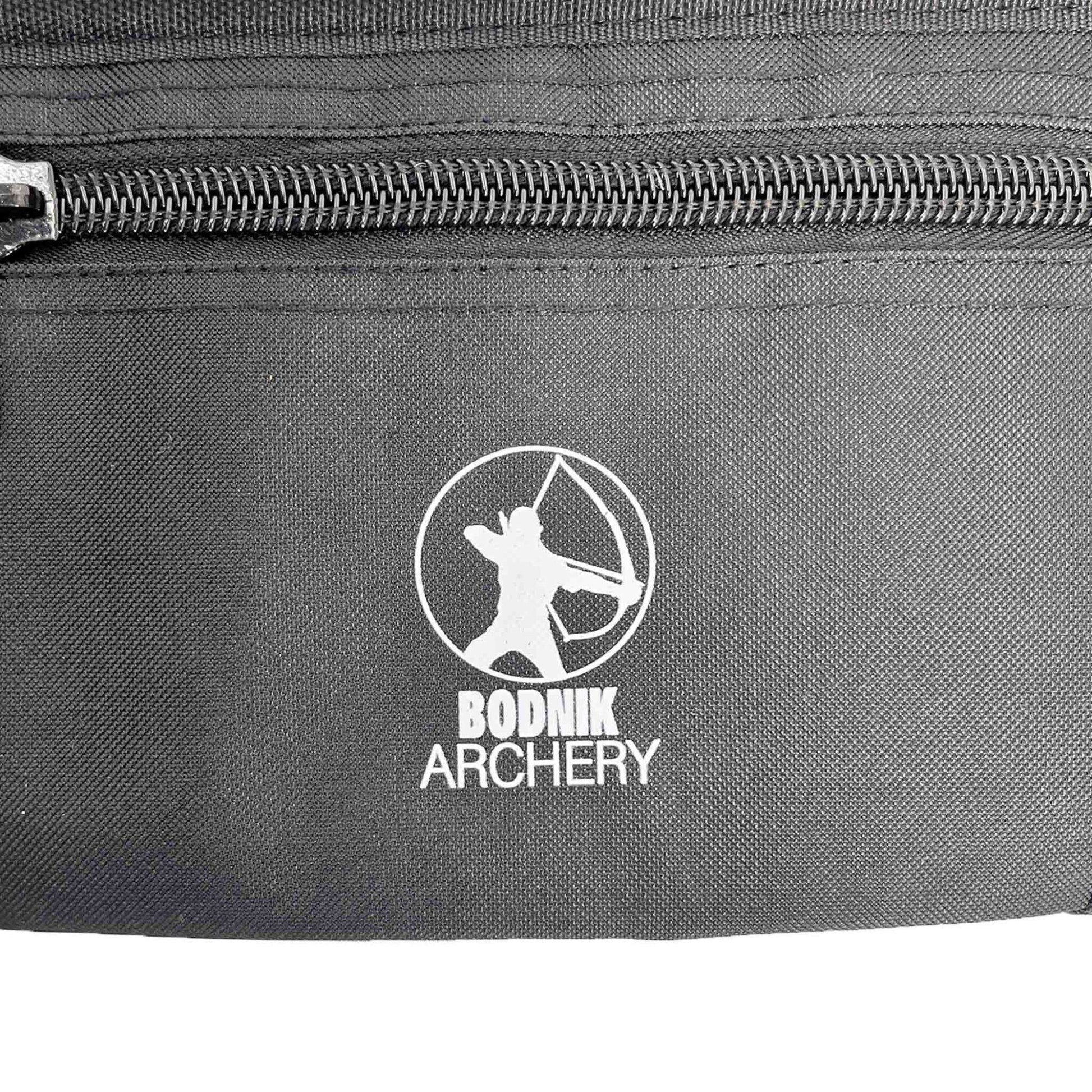 Schwarzer Stoff mit sichtbaren Nähten sowie ein Reißverschluss. Mittig ein weißes Logo, das eine stilisierte Figur mit gespanntem Bogen im Kreis darstellt. Darunter der Schriftzug "BODNIK ARCHERY".