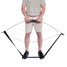 Ein Mann trägt beigefarbene Shorts und ein T-Shirt, steht mit schwarzen Sportschuhen auf einem schwarzen Gurt, hält einen Bogen mit beiden Händen. Der Gurt ist an den Enden des Bogens befestigt.