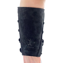 Ein schwarzer Armschutz aus Wildleder sitzt am Unterarm einer Person, seitlich mit mehreren Knöpfen verschlossen, Logo und Schriftzug sichtbar.