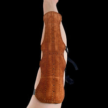Ein Unterarm mit einem braunen Lederarmschutz, längliches Design, dekorative Nähte, schwarze Riemen zur Befestigung.