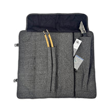 Eine offene, graue Filztasche mit mehreren Fächern. Zwei Holzteile, vermutlich Wurfarmteile eines Bogens, stecken in mittleren Taschen. Rechts ist ein Griffstück eines Bogens mit auffälligem Muster sichtbar. In einer weiteren Tasche befinden sich mehrere Dokumente und ein durchsichtiger Plastikbeutel. Klappverschlüsse an den Seiten.